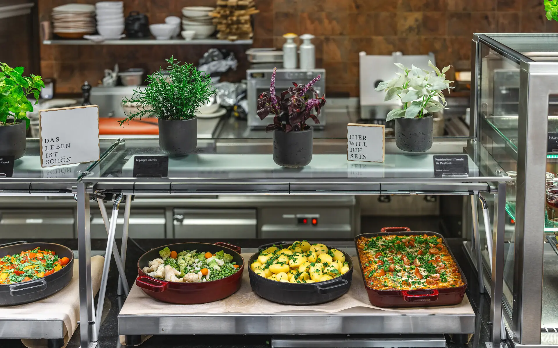 Abendessen aja Bad Saarow Ein Hauptspeisenbuffet mit Auflauf, Gemüse und Kartoffeln. Kleine Schilder und dekorative Kräuter unterstreichen den gemütlichen und gesunden Flair.