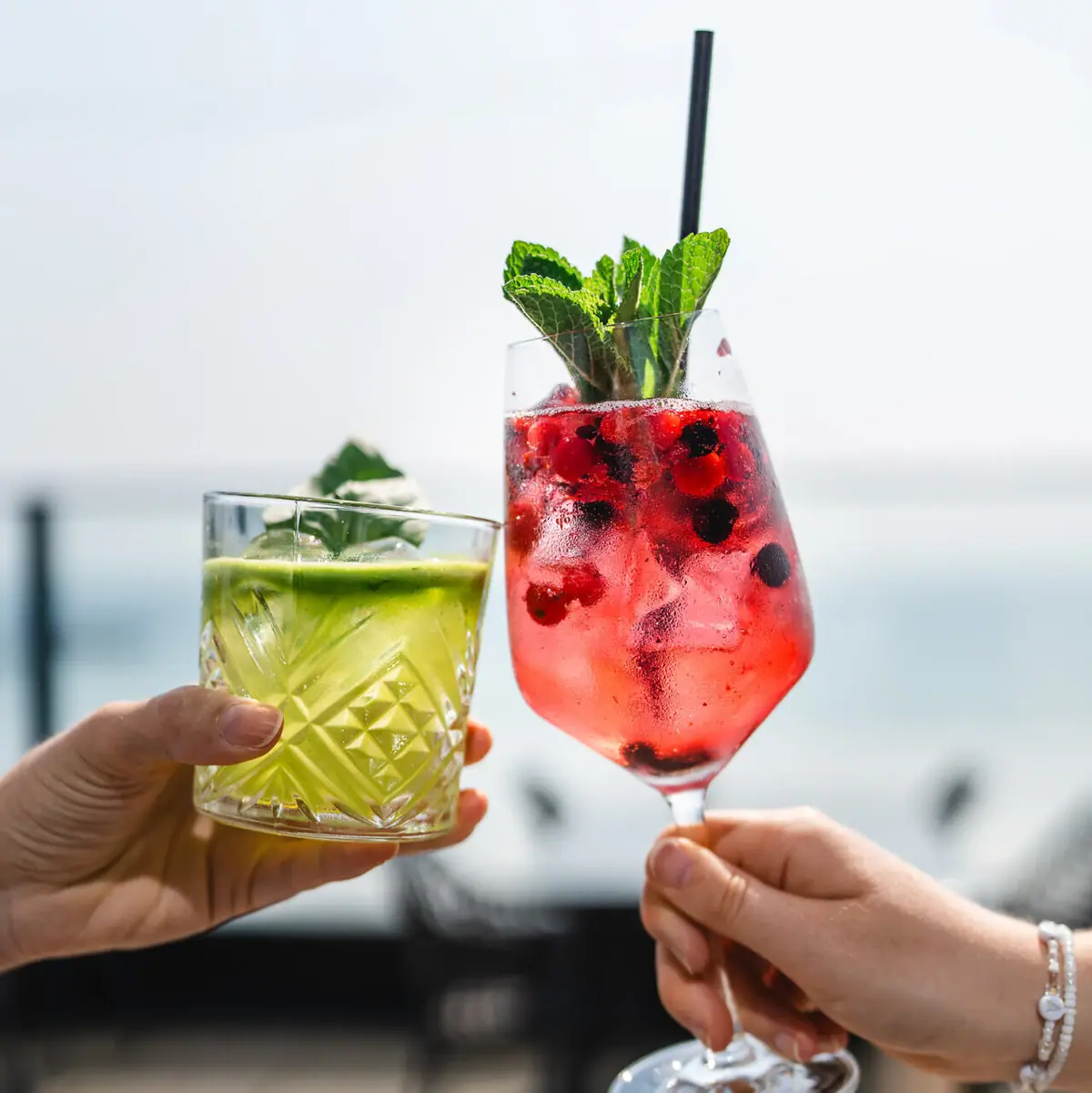 Cocktails Ein Paar Hände hält Cocktails mit Fruchtgarnitur.