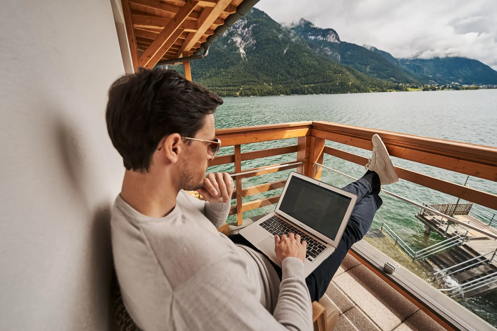 Mann sitzt mit einem Laptop auf dem Schoß auf einer Veranda.