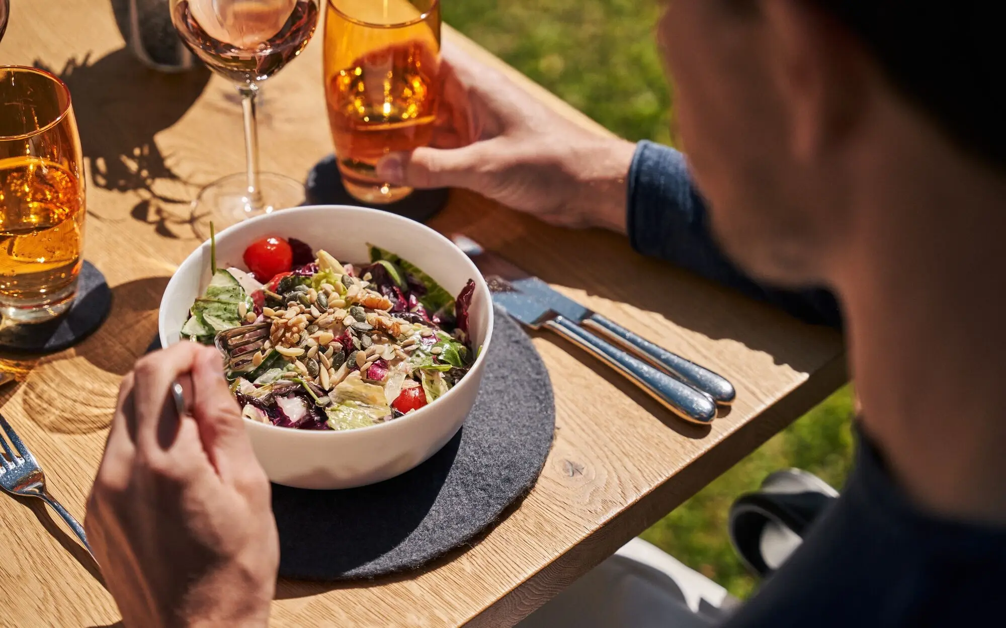 Mann isst Salat und trinkt Wein am Tisch.