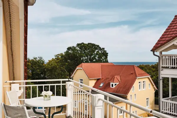 Nordperd & Villen Göhren Ein Balkon mit Tisch, einem Haus und Bäumen im Hintergrund.