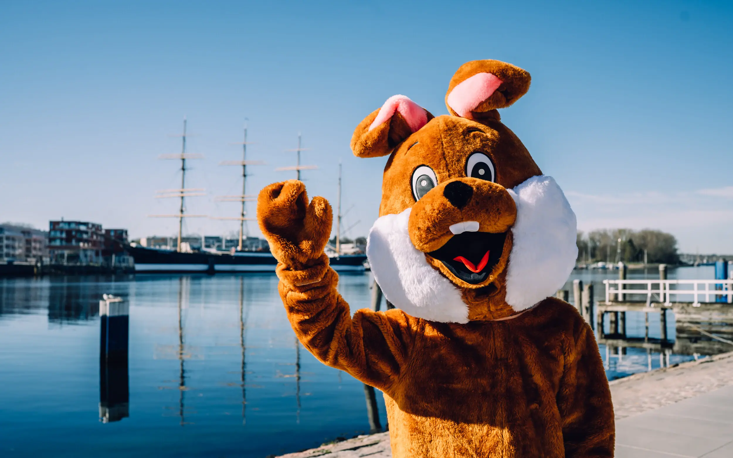 Ostern bei aja Eine person in einem großen Hasenkostüm steht am Wasser und winkt in die Kamera.