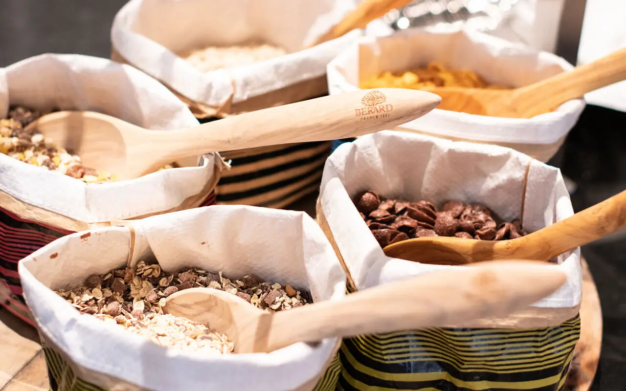 Müsli Mehrere bunte Behälter mit verschiedenen Müslisorten und Cerealien mit großen Holzlöffeln stehen auf einem runden Holztablett.