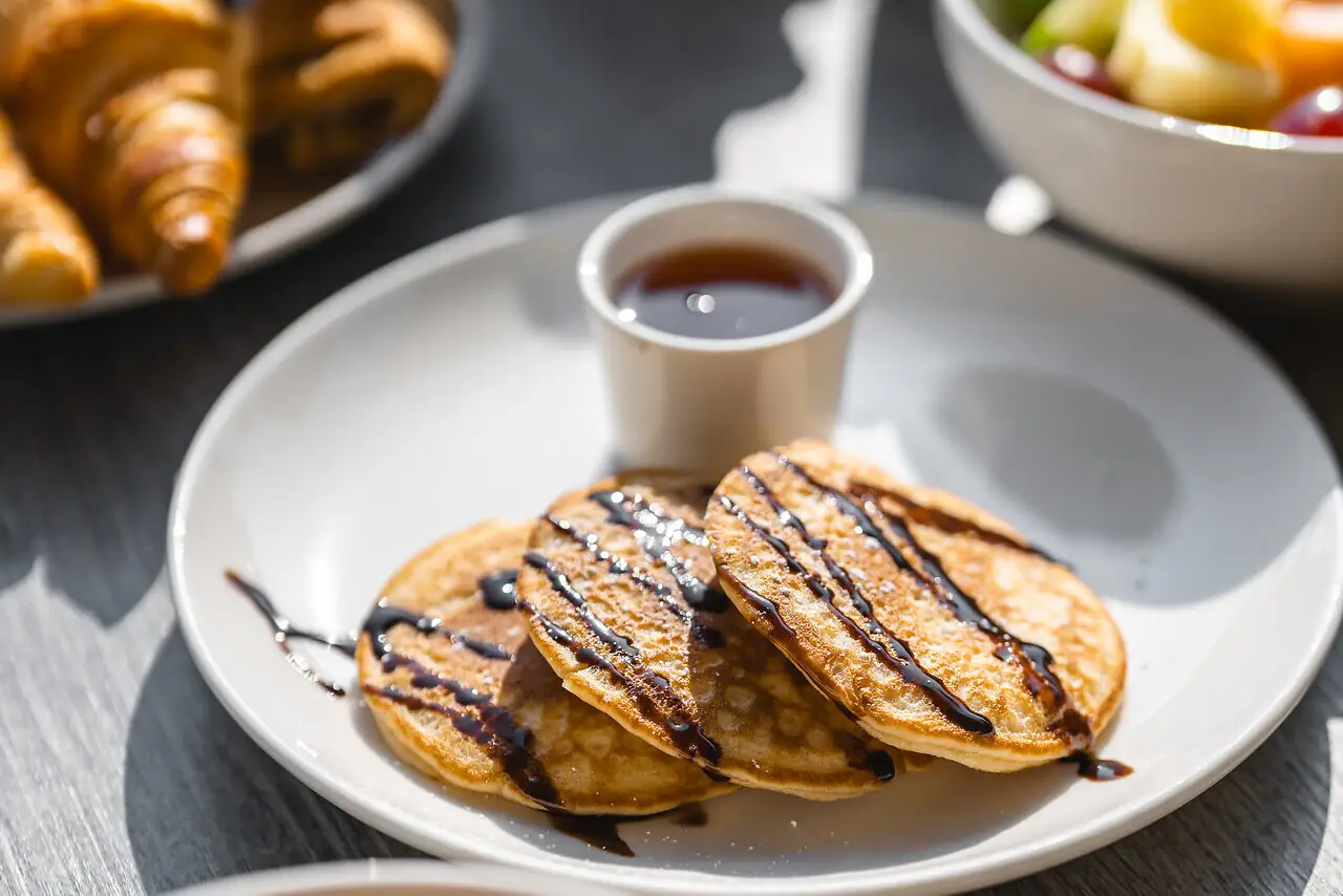 Eierspeisen Ein Teller mit Pfannkuchen und Sirup sowie eine Tasse mit Sirup.