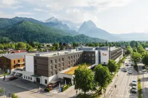 aja Garmisch-Partenkirchen Ein Gebäude mit Bäumen und Bergen im Hintergrund.