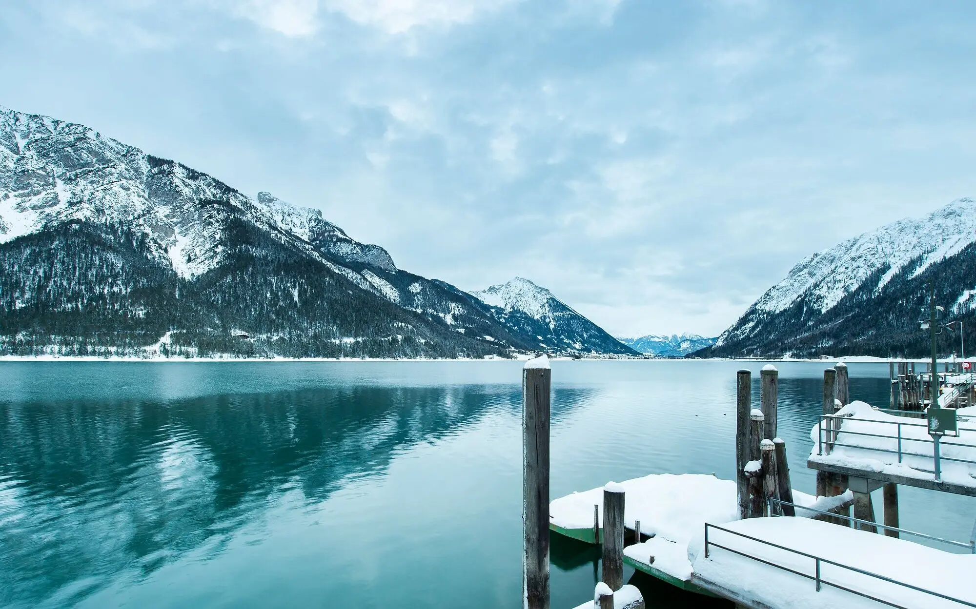 Schneebedeckter Steg am Achensee mit Bergen im Hintergrund.