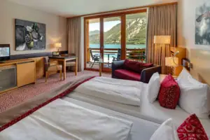 Doppelzimmer Ein Raum mit zwei Betten, einem Tisch und Stühlen, Blick auf einen See.