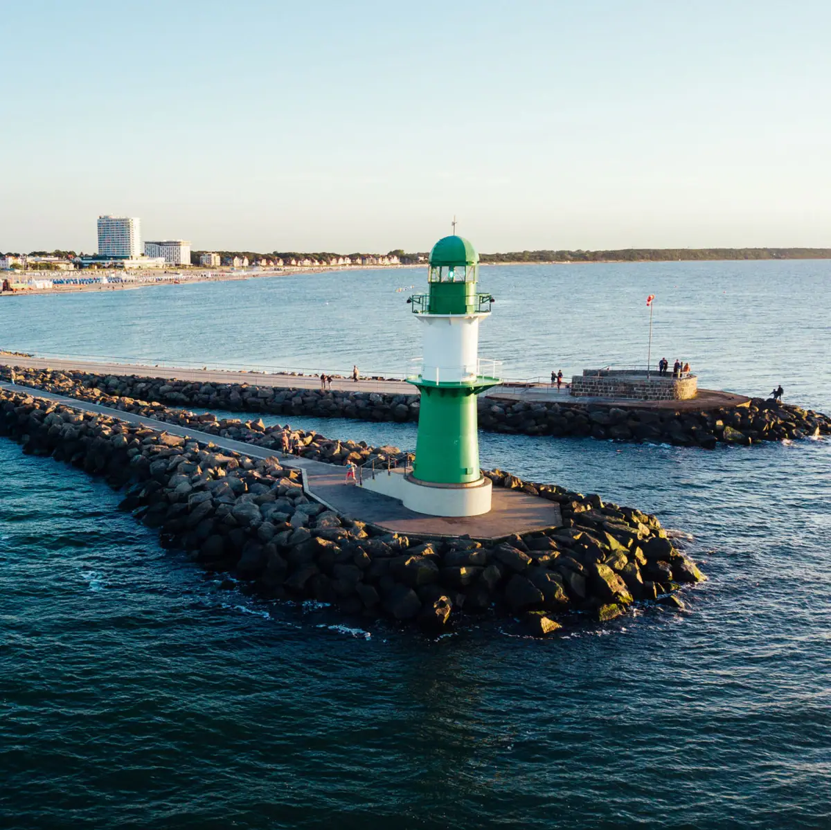 Warnemünde Ein grün-weißer Leuchtturm auf Felsen im Wasser.