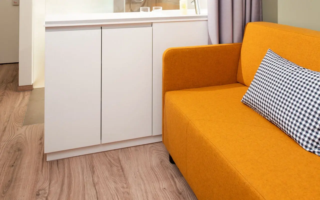 Eine Sofaecke in einem Hotelzimmer mit einem senfgelben Sofa vor einer hell grünen Wand.