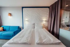 Doppelzimmer Komfort Landseite Ein Bett mit weißen Laken und ein blauer Couch.