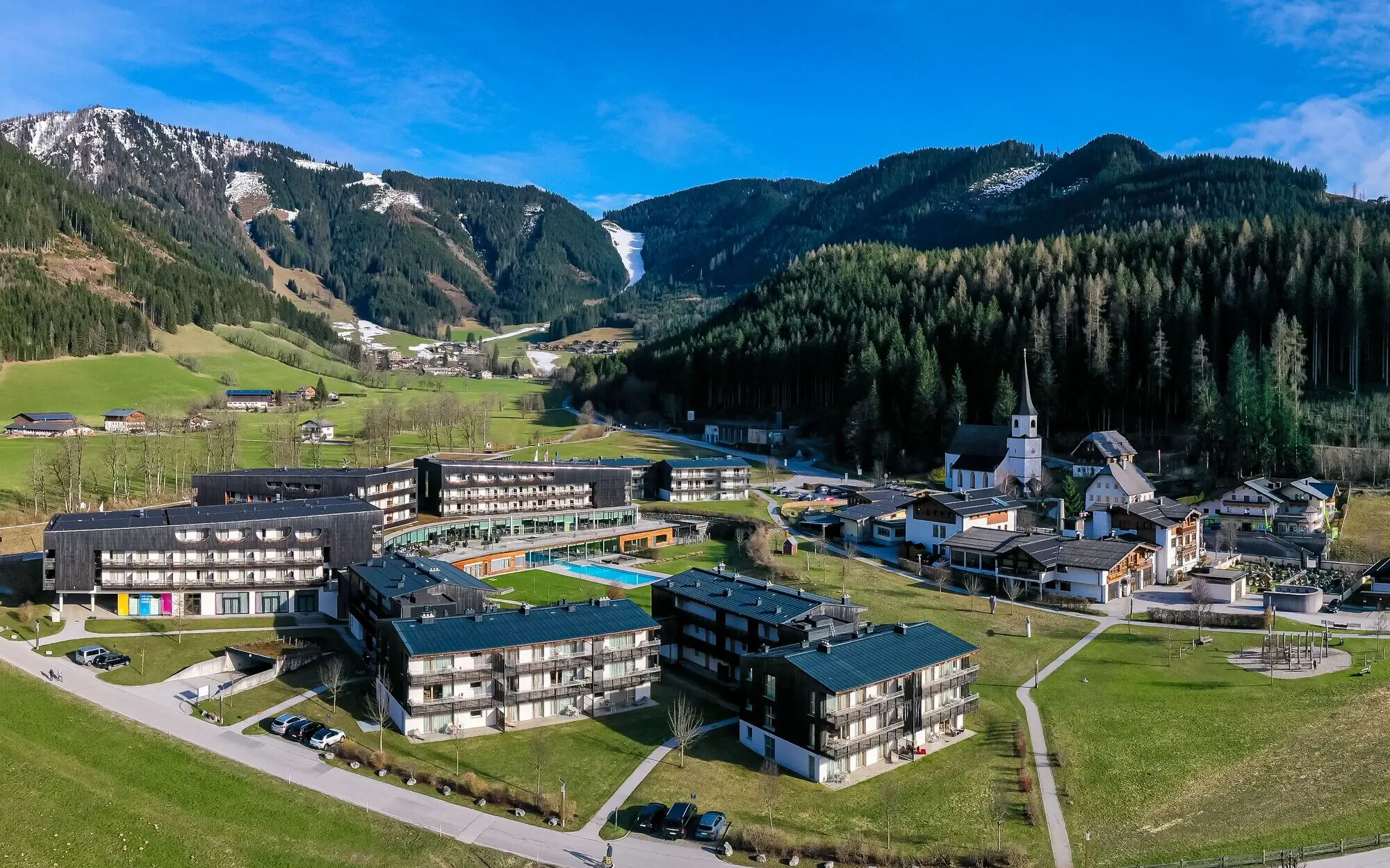 aja Resort Werfenweng Das aja Werfenweng mit Rasenfläche und Swimmingpool umgeben von Bäumen und Bergen.