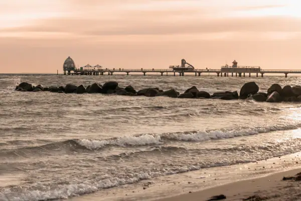 Strand vom Grömitz Strand mit einem Pier und Felsen bei Sonnenuntergang.
