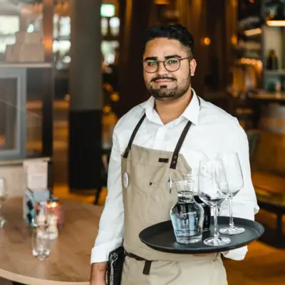 Servicepersonal Ein Mann hält ein Tablett mit Weingläsern und einer Flasche.