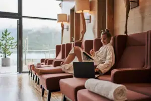 SPA-Bereich Eine Frau in einem weißen Bademantel sitzt mit einem Laptop auf einem Sofa.