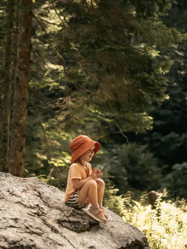 Mädchen sitzt auf einem Stein Ein Kind sitzt auf einem Felsen im Wald.