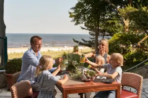 Ausblick Terrasse Eine Familie mit 2 Kindern sitzt an einem Tisch mit Getränken und Blick auf das Meer.
