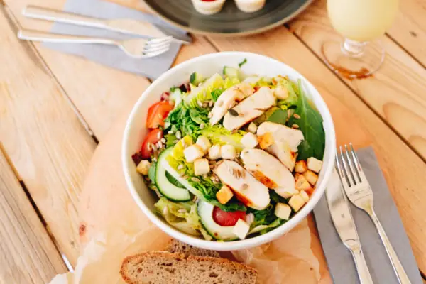 Salat mit Hähnchen Ein Teller mit Essen und ein Getränk auf einem Tisch.