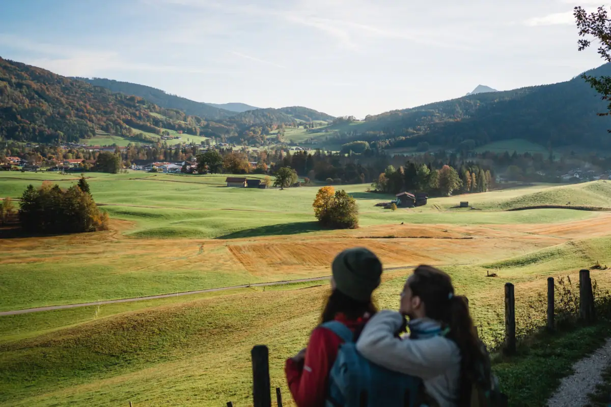 Ruhpolding Zwei Personen betrachten eine Landschaft mit Bäumen und Wolken am Himmel.