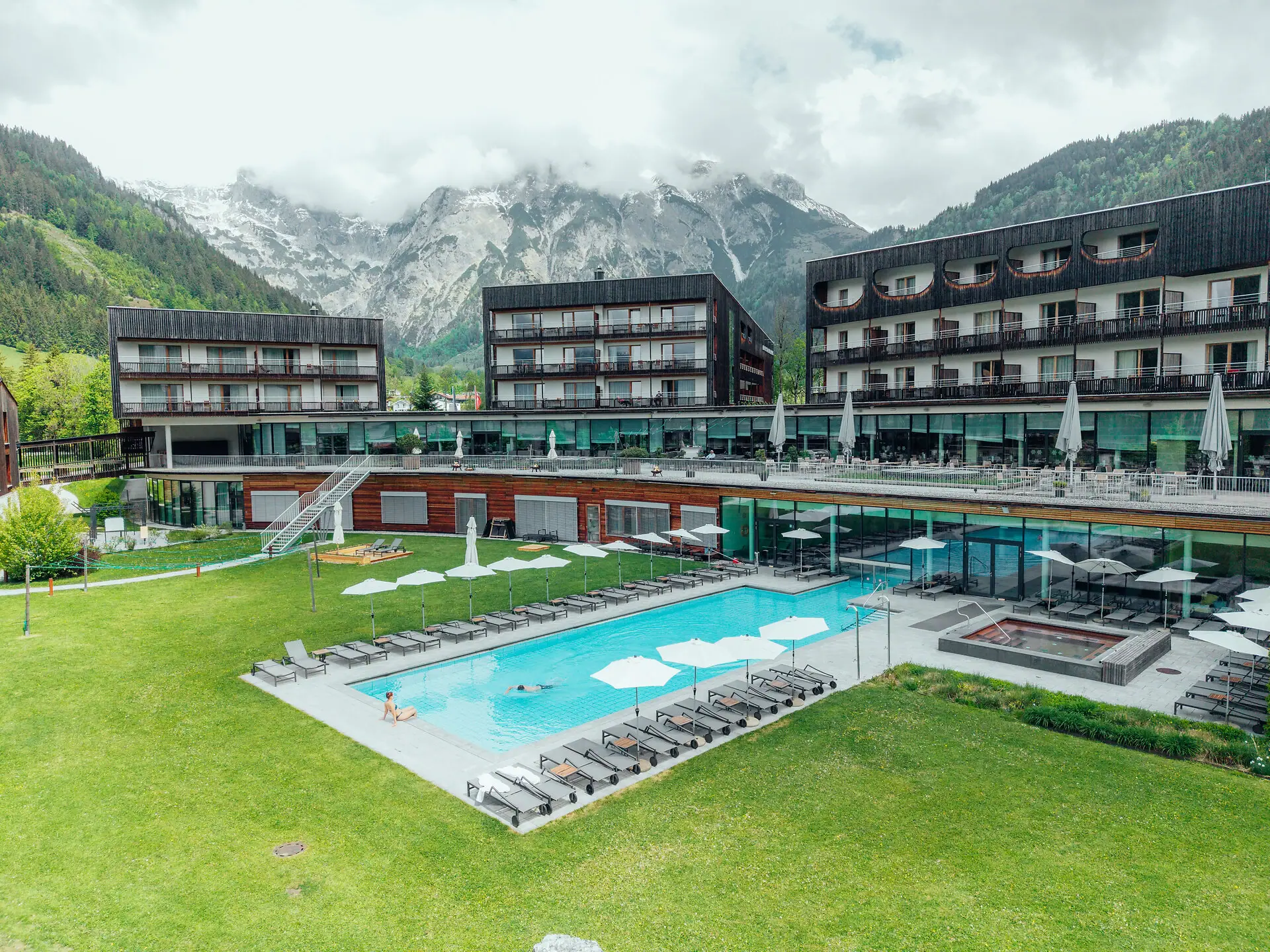 aja Bergresort Werfenweng Ein Außenpool in einem Hotel mit Rasen und Bergen im Hintergrund.