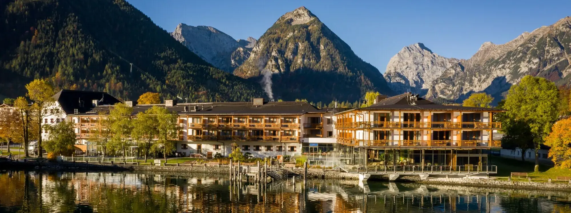 aja Fürstenhaus am Achensee Ein Gebäude neben einem Gewässer mit Berglandschaft im Hintergrund.