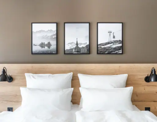 Bett mit Kissen Ein Bett mit weißen Kissen und einem hölzernen Kopfteil, darüber ein Bild von einem Berg und einem Skilift.