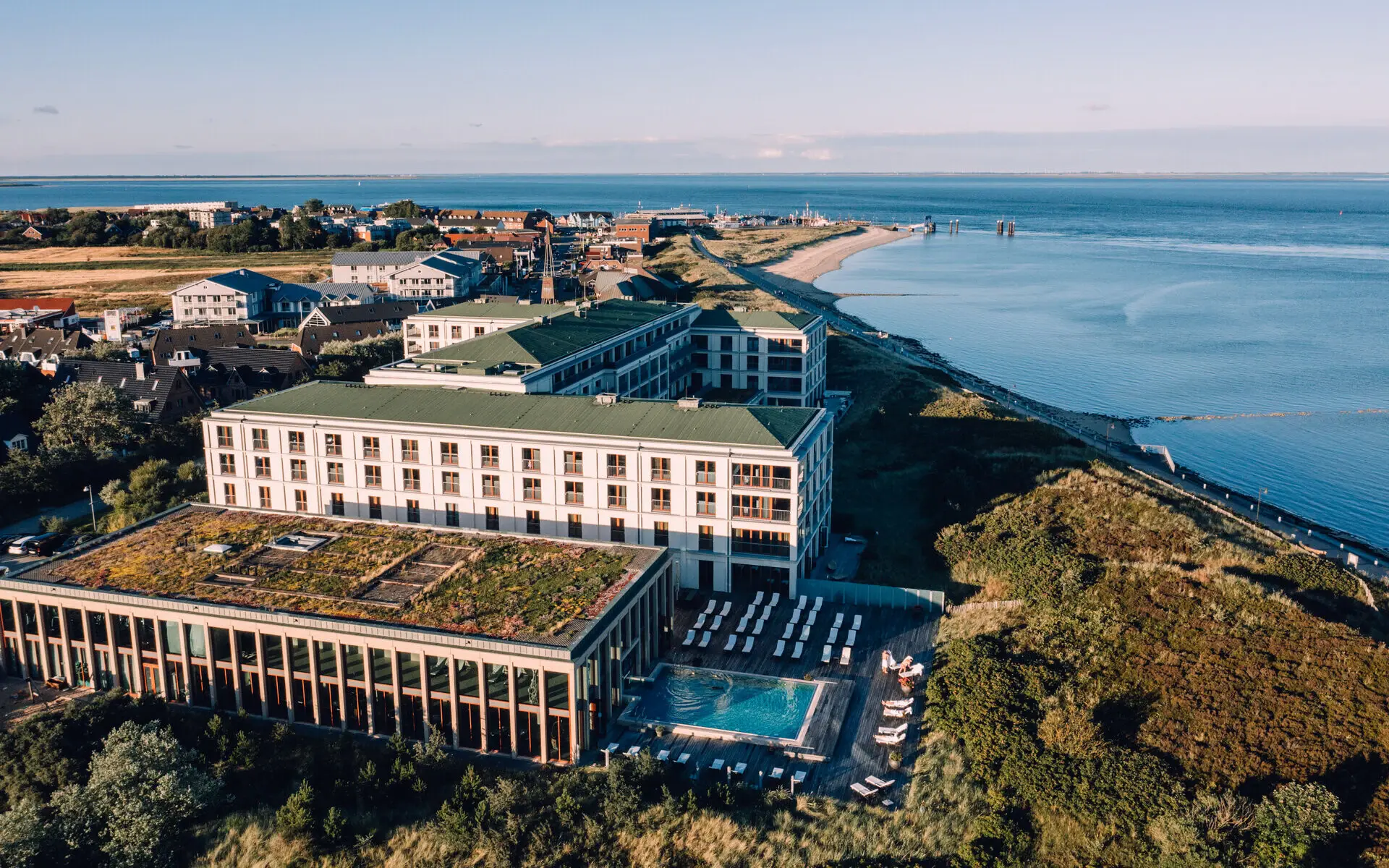 A-ROSA Sylt Vogelperspektive auf das A-ROSA Sylt, gelegen inmitten der Dünenlandschaft mit Blick auf die Nordsee, einer begrünten Dachterrasse und einem Außenpool, umgeben von der idyllischen Inselatmosphäre.