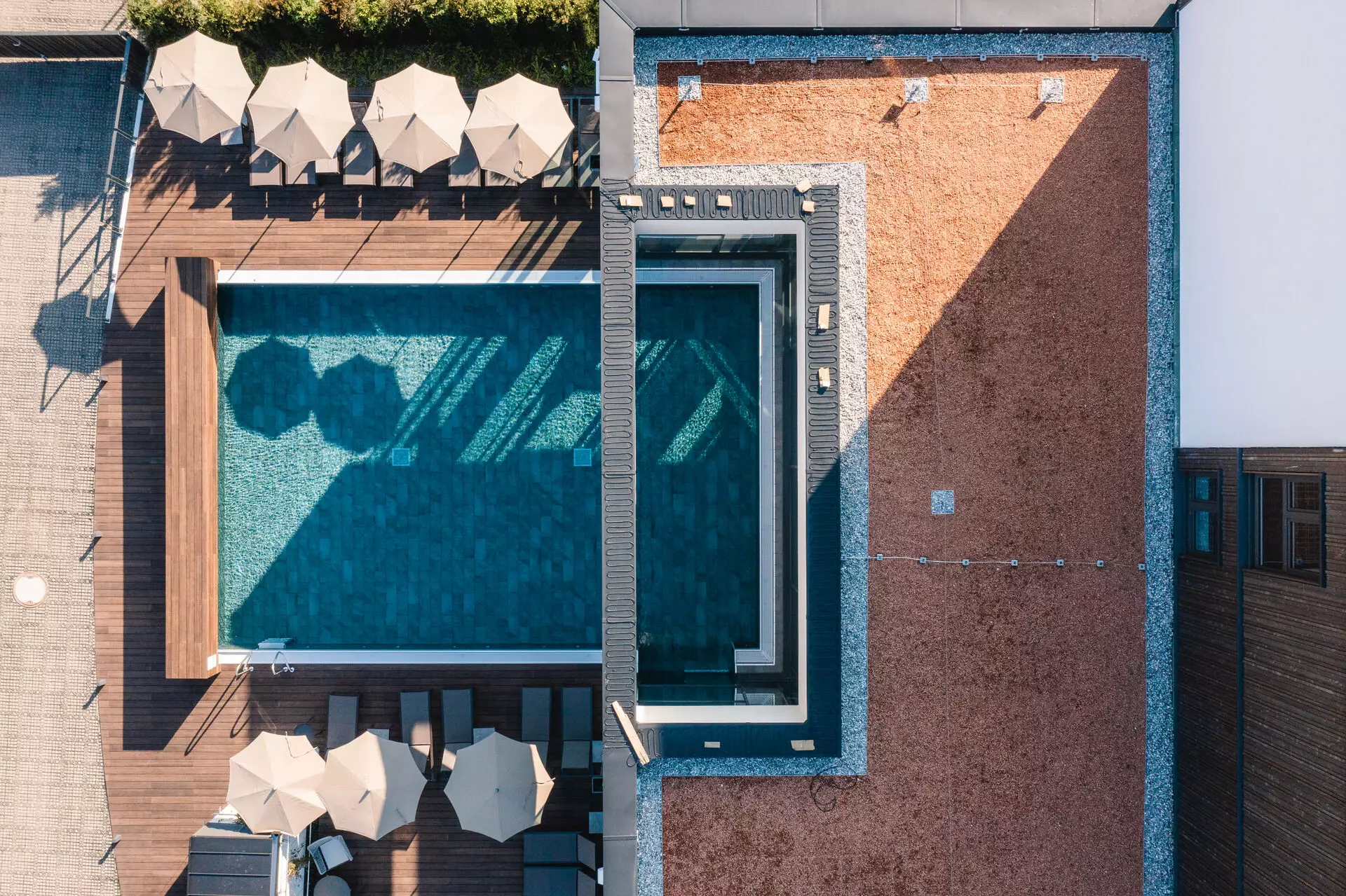 Vogelperspektive auf einen modernen Hotelpool mit umliegenden Liegestühlen und Sonnenschirmen.
