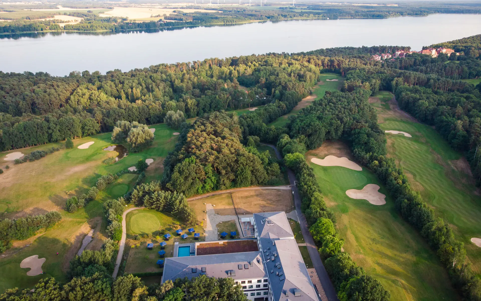 Eine Luftansicht eines großen Gebäudes, umgeben von Golfplätzen, Wäldern und einem einem großen See im Hintergrund.