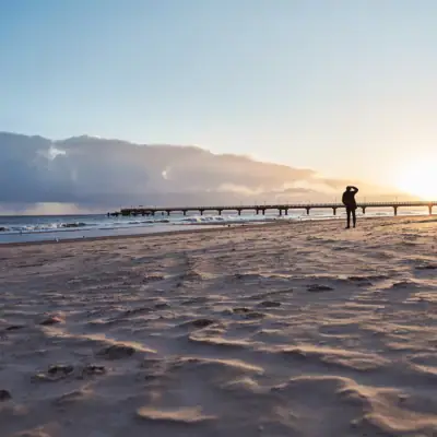 Eine Person geht am Strand entlang unter einem bewölkten Himmel.