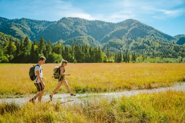 Wandern in Ruhpolding Ein Mann und eine Frau gehen in einem Feld mit Bergen im Hintergrund.