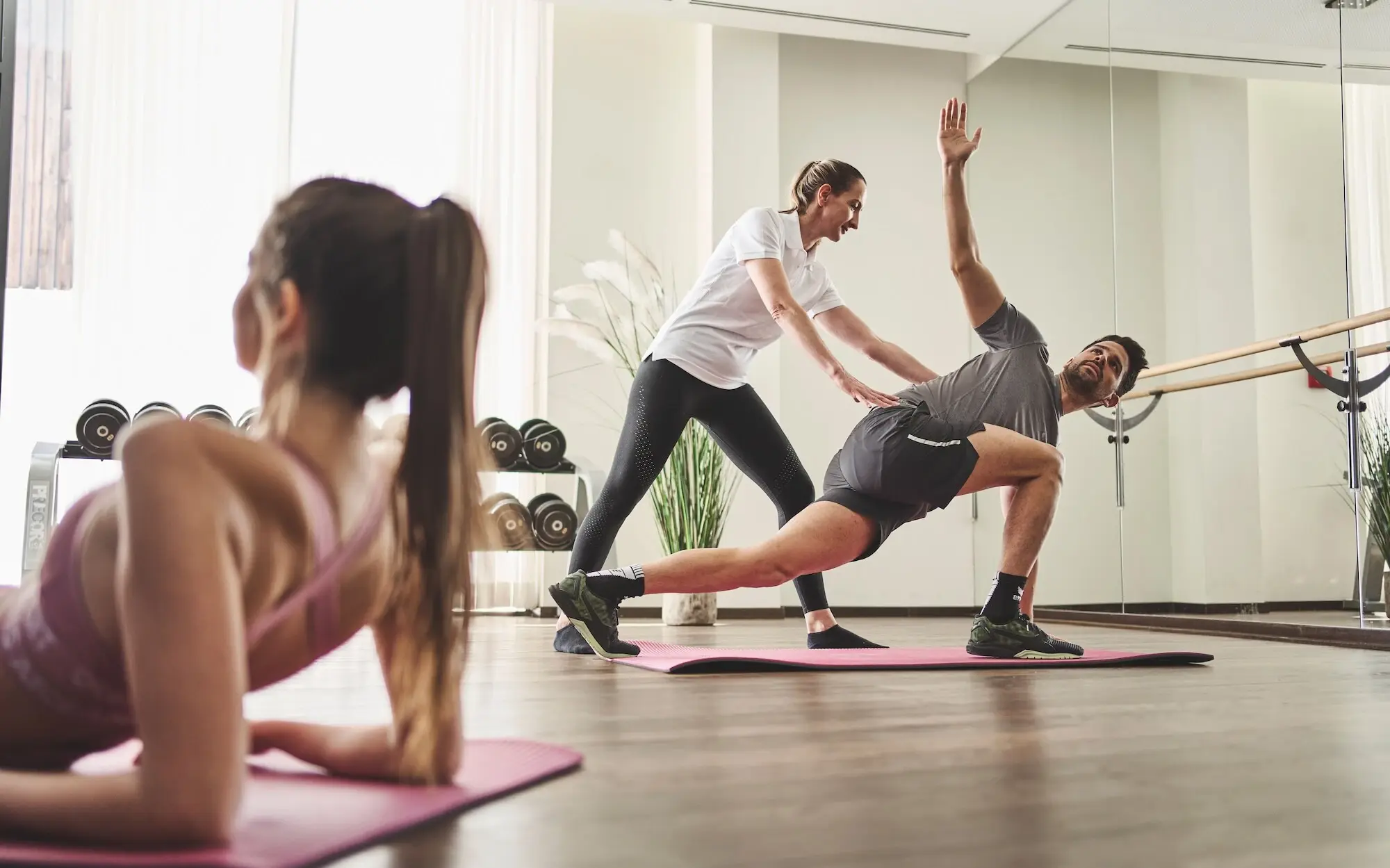 Kurse aja Werfenweng Ein Mann dehnt sich auf einer Yogamatte in einem Kursraum, während eine Frau ihm Anweisungen und Hilfestellung gibt.