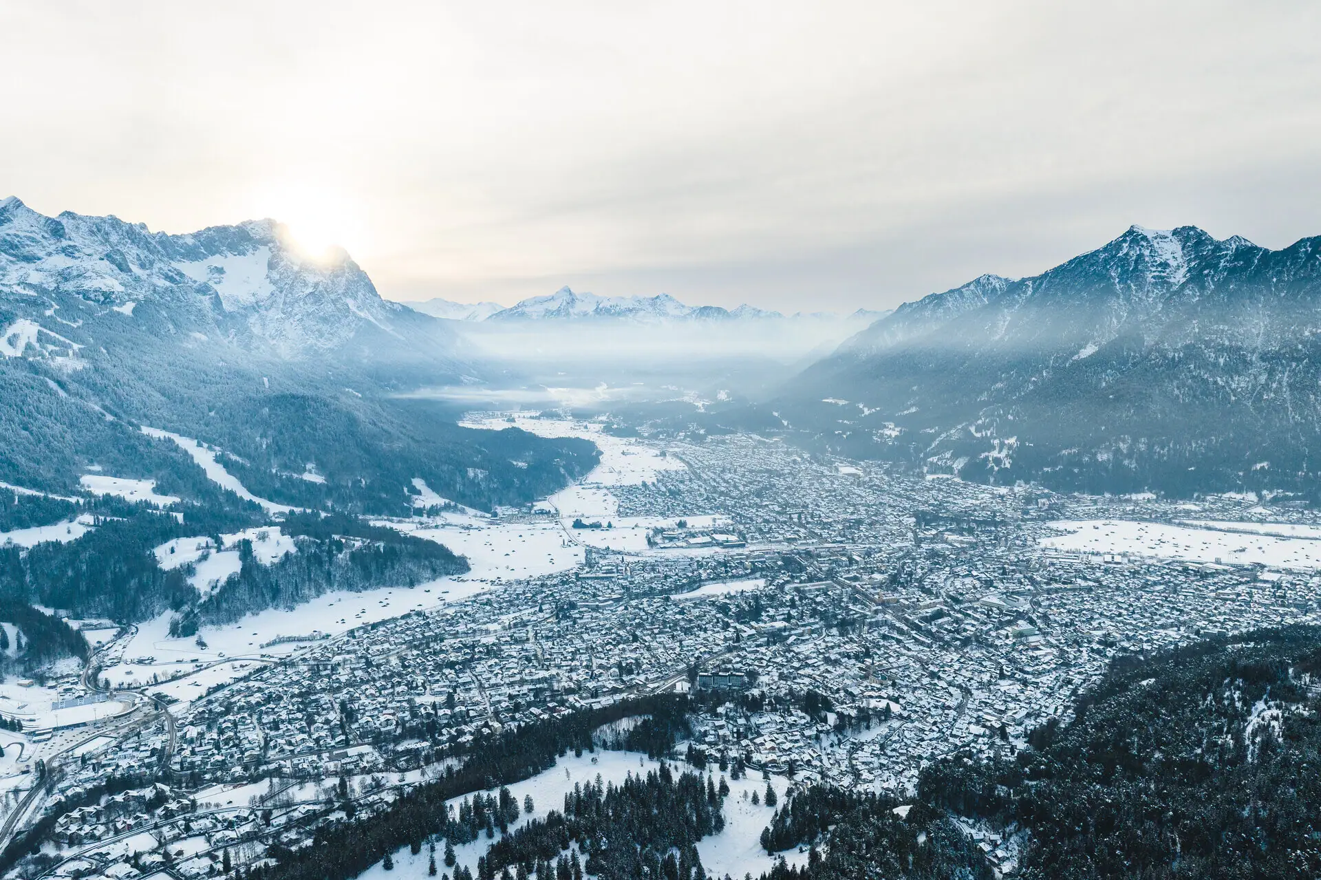 Anreise Flugzeug Schneebedeckte Stadt mit Berglandschaft im Hintergrund.