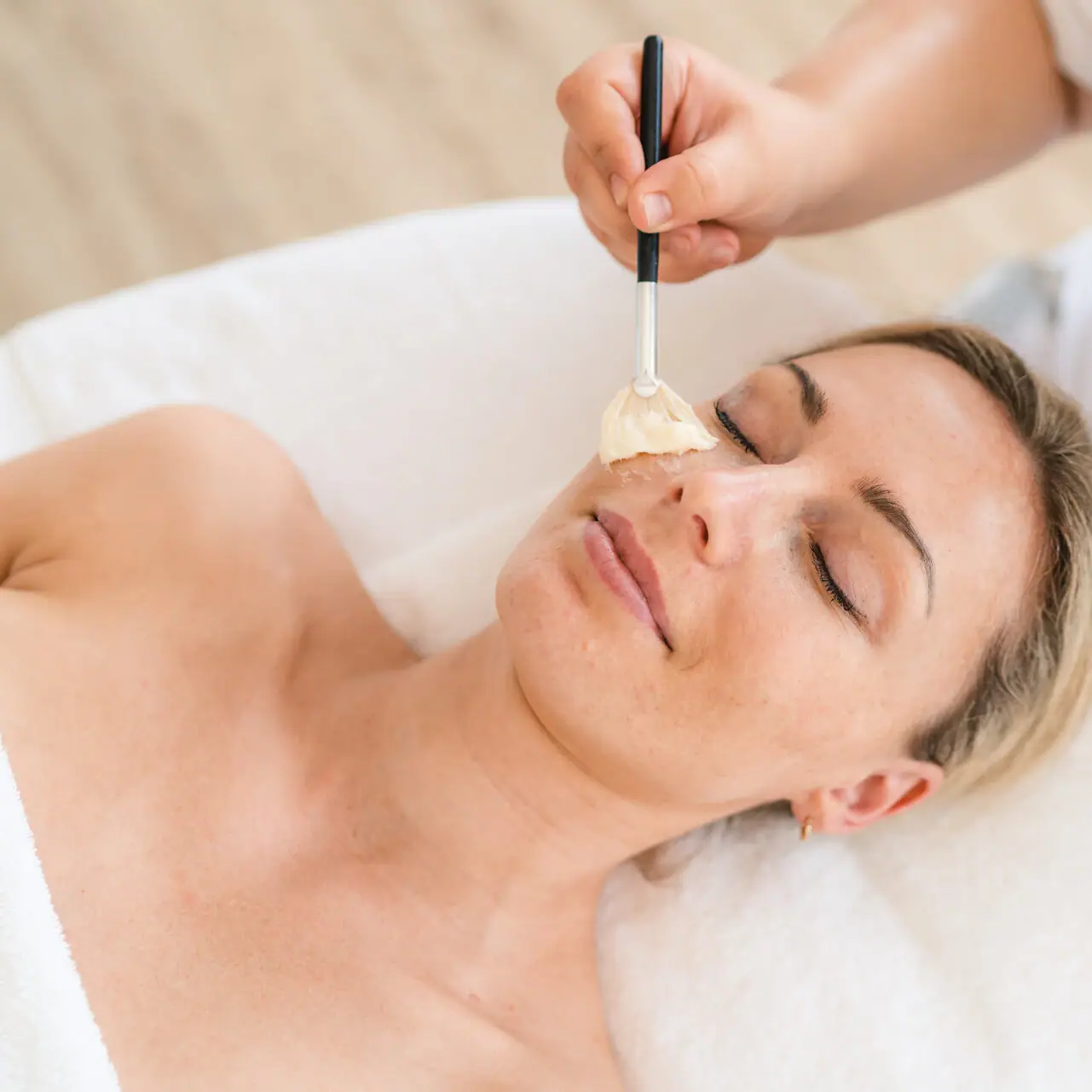 Wellnessanwendungen in Ruhpolding Eine Frau liegt mit einem Pinsel im Gesicht.