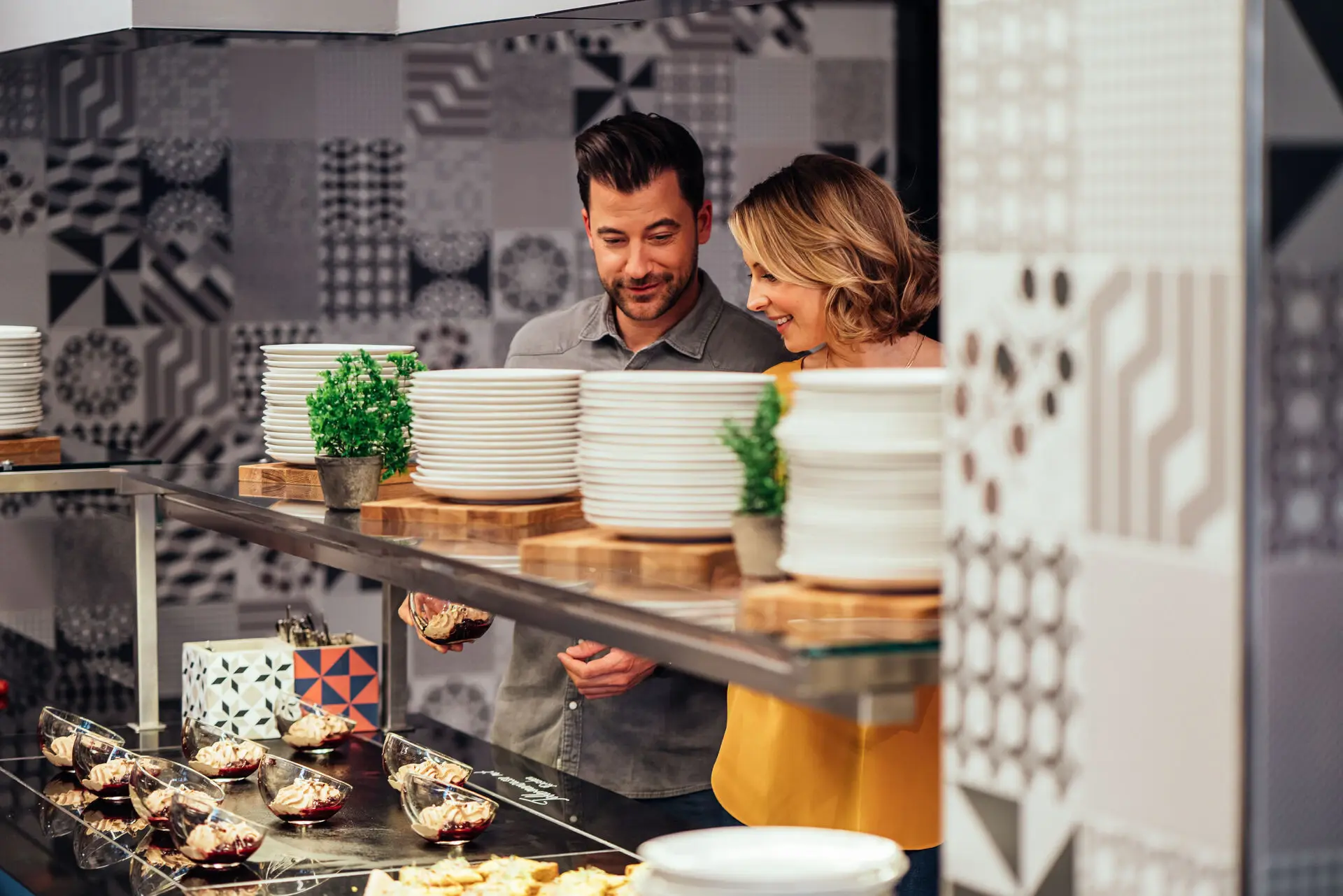 aja Zürich Buffet Ein Paar steht lächelnd vor dem Buffet im aja Zürich, umgeben von modernem Design und köstlich angerichteten Speisen.