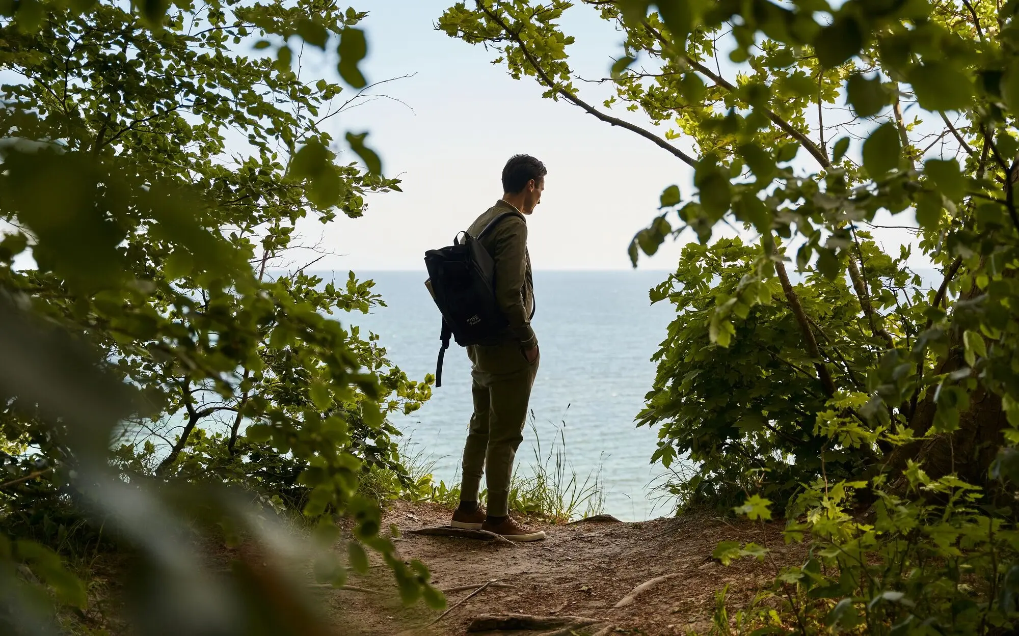 Mann mit Rucksack steht auf einem Hügel mit Blick auf die Ostsee.