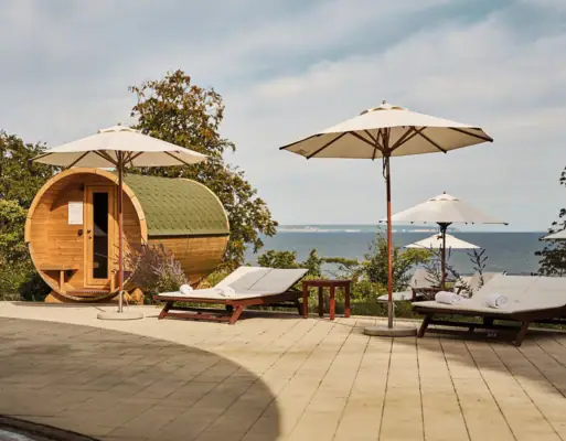 Außenbereich Wellness Deckstühle und Sonnenschirme neben einem Fass und einem Gewässer.