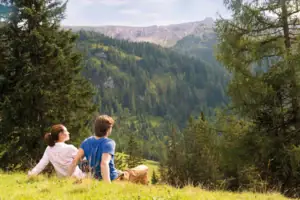 Ausblick Ein Mann und eine Frau sitzen auf einem Hügel und schauen auf einen Berg.