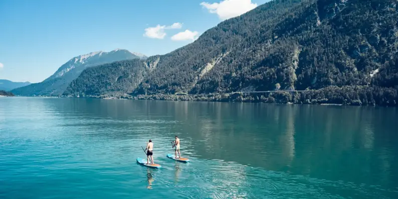 Zwei Personen auf Paddleboards auf einem See mit Bergen im Hintergrund. Zwei Personen auf Paddleboards auf einem See mit Bergen im Hintergrund.