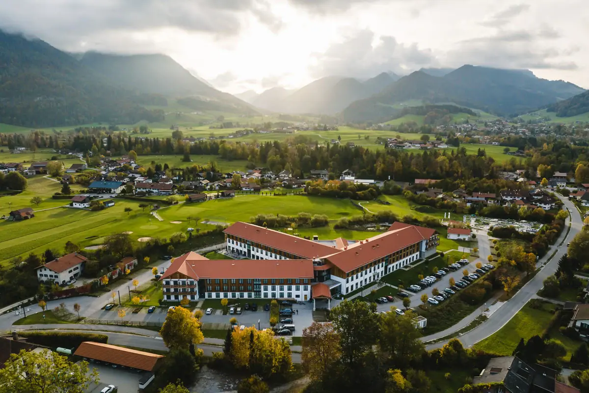 aja Ruhpolding Ein Gebäude mit einem Parkplatz in einem Tal, im Hintergrund Berge.