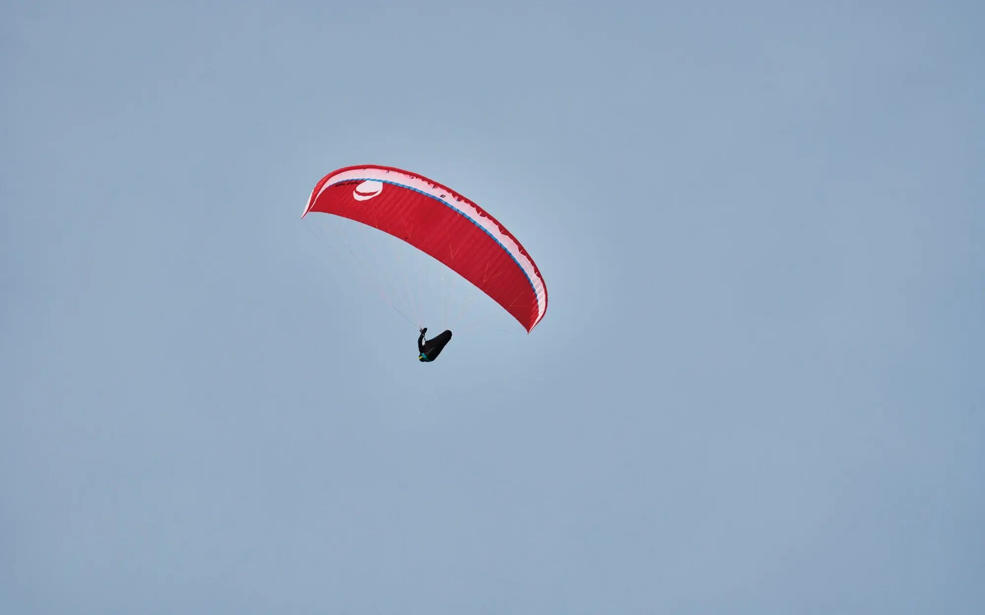 Paragleiten Werfenweng Person beim Paragliden schwebt mit einem roten Schirm vor dem bleuen Himmel.