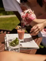 Person sitzt an einem Tisch mit einem Getränk auf einer Zeitung.