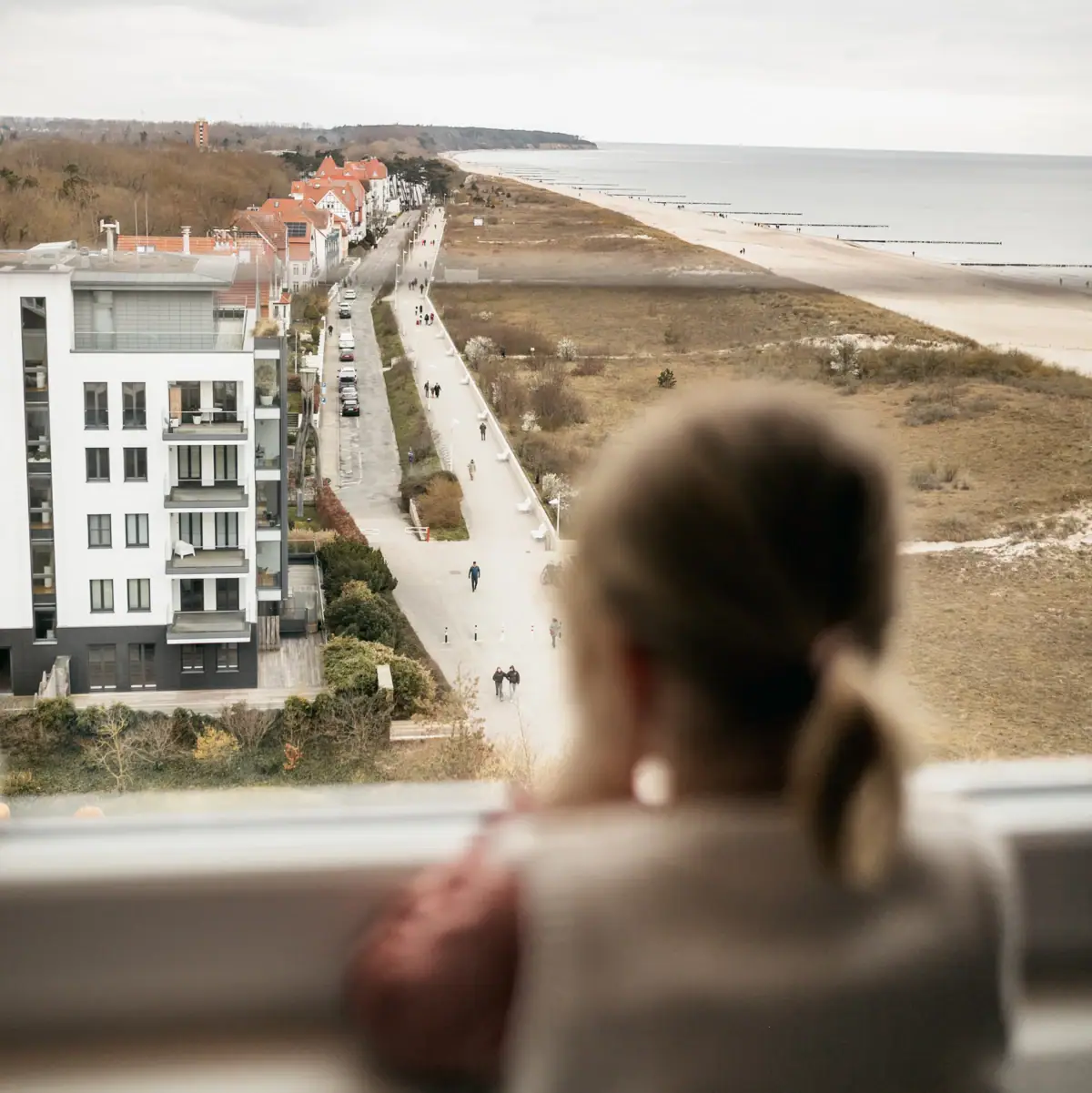 Mädchen guckt aus dem Fenster Eine Frau schaut aus einem Fenster auf einen Strand.