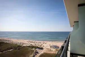 Suite im aja Warnemünde Aussicht vom Balkon. Strand mit Menschen, Himmel und Wolken im Hintergrund.