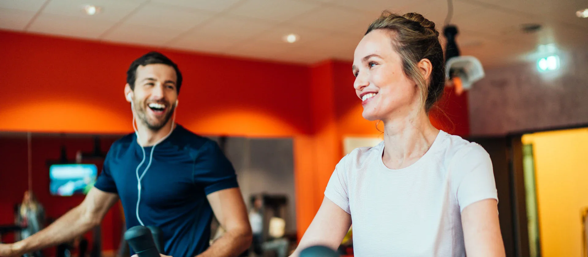 Ein lächelndes Paar trainiert gemeinsam auf Crosstrainern in einem modernen Fitnessstudio mit freundlicher Atmosphäre.