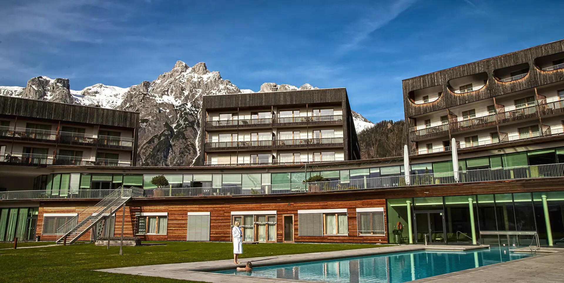 aja Bergresort Werfenweng Eine Person steht vor einem Schwimmbecken und dem Hotel im Freien.