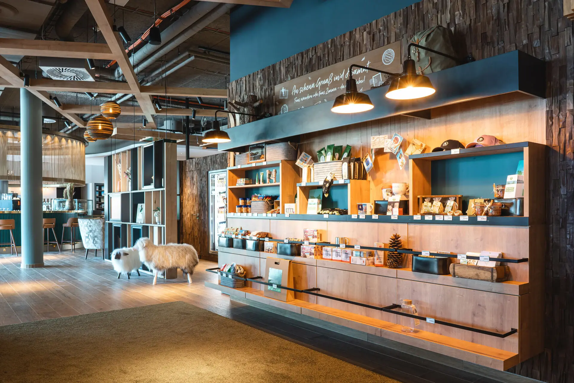 Shop aja Garmisch-Partenkirchen Stilvoller Shop-Bereich in einem Hotel mit einer Auswahl an regionalen Produkten und Souvenirs. Die Holzregale sind mit verschiedenen Artikeln wie Hüten, Kosmetikprodukten und Snacks bestückt. Im Hintergrund ist eine Bar zu sehen.