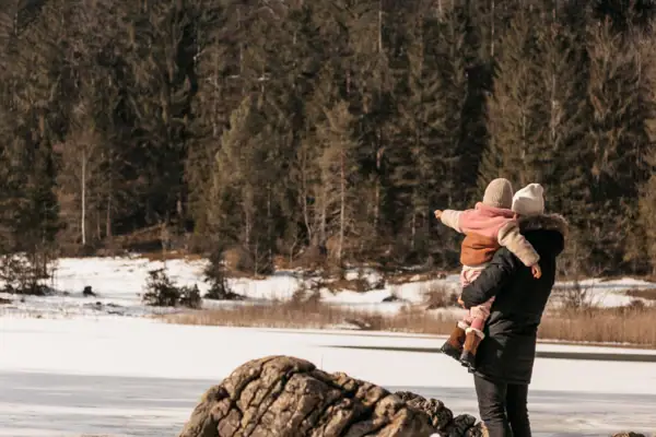 Familie im Winterurlaub Ein Mann trägt ein Kind auf seinem Rücken im Schnee.