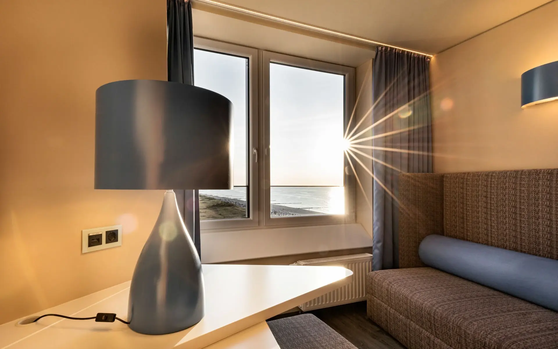 Ein gemütliches Zimmer, im Vordergrund steht eine Lampe, im Hintergrund ist ein schöner Ausblick aus einem Fenster