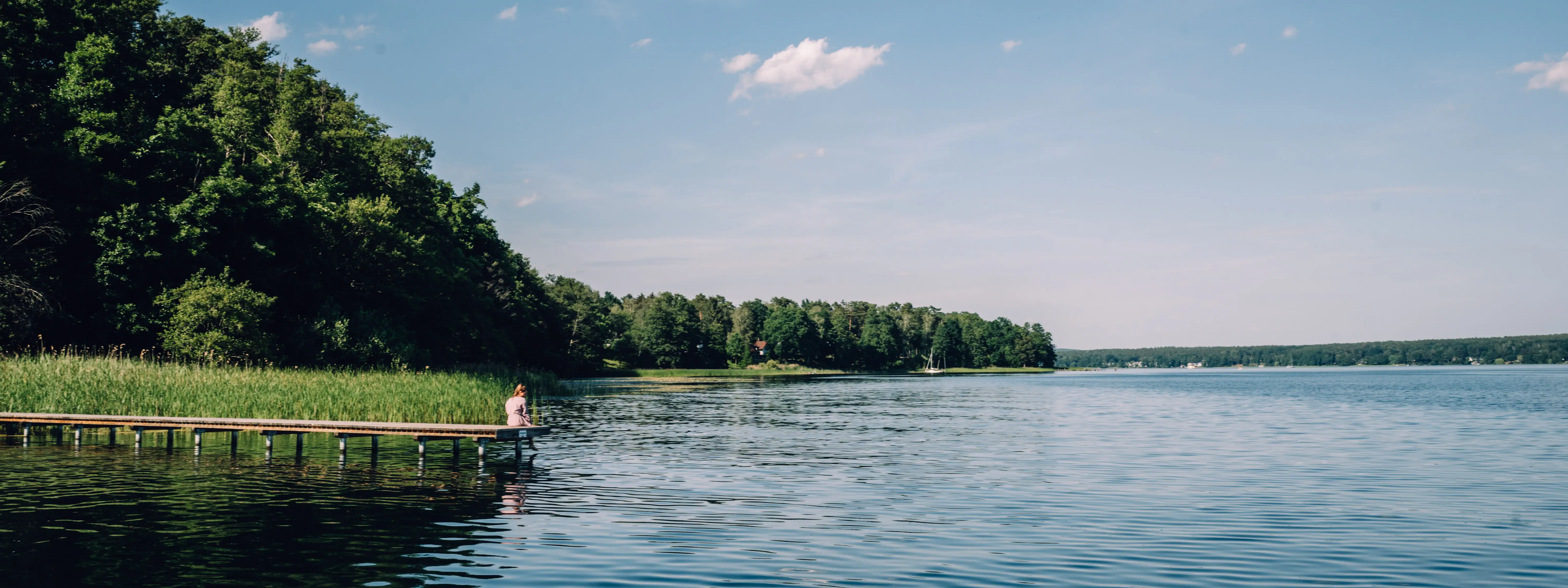 Steg am See Eine Person sitzt auf einem Steg an einem Gewässer.