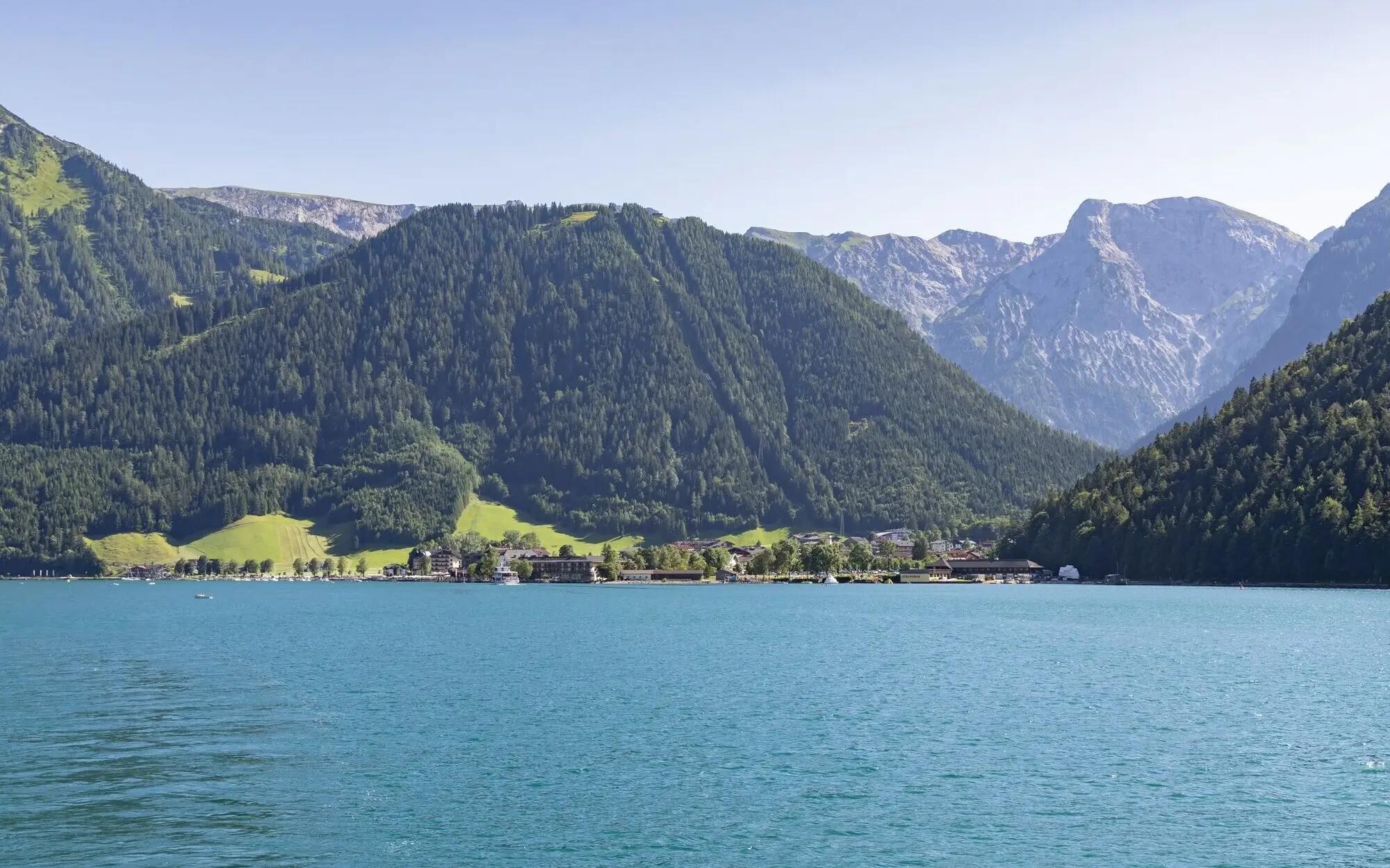 Blick auf den Achensee mit umliegenden Bergen und klarem Himmel.